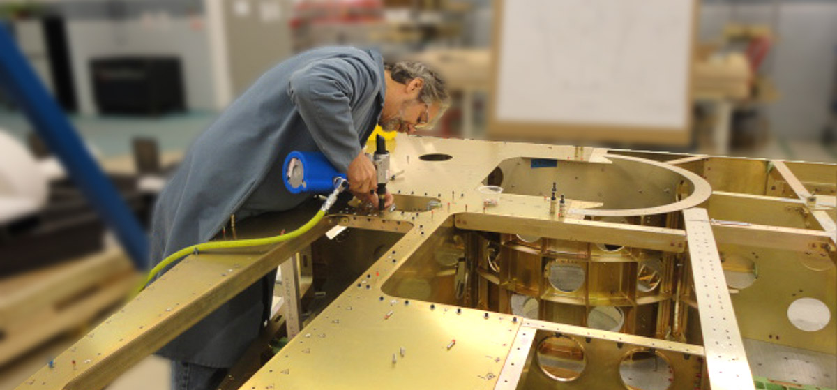 Worker uses a pneumatic riveter to fasten an aluminum structure during sheet metal assembly.